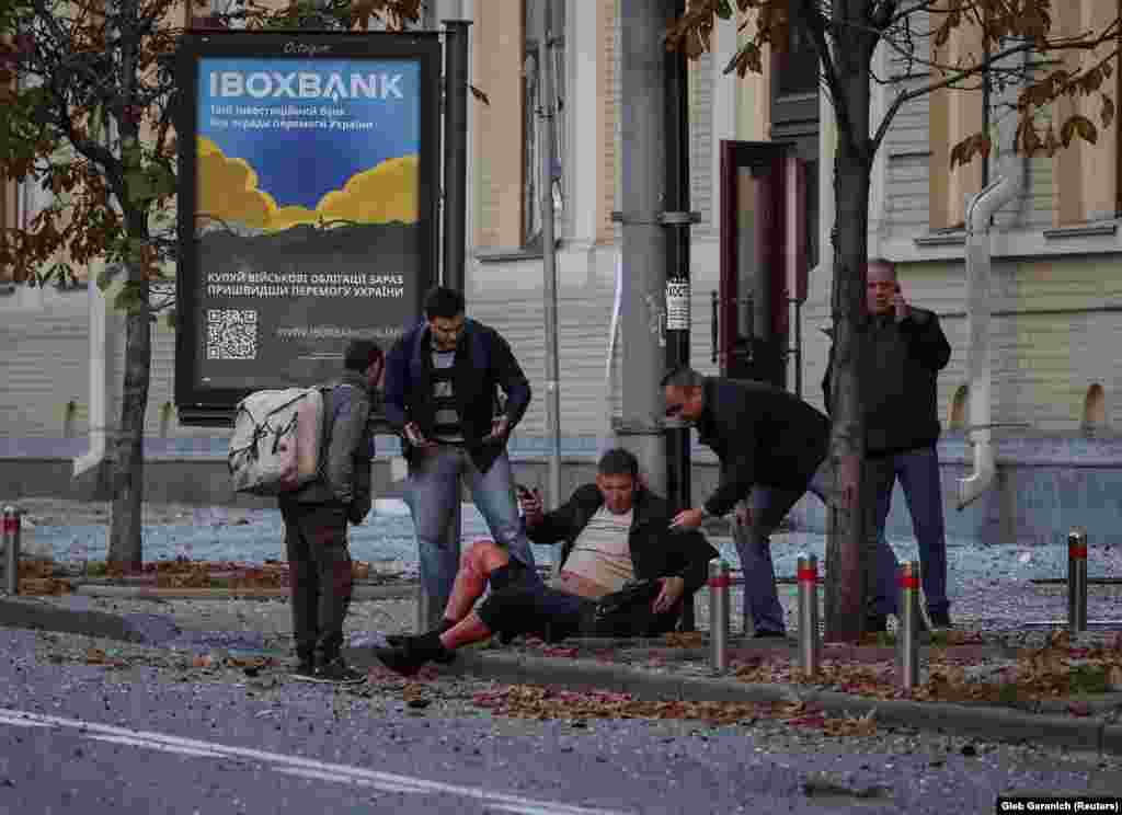 Câțiva oameni ajută un bărbat rănit, căzut pe o stradă din centrul Kievului.