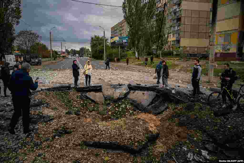 Жители смотрят на воронку, образовавшуюся после ракетного удара по Днепру, 10 октября. Президент России Владимир Путин назвал ракетные удары &laquo;ответом&raquo; на взрыв на Крымском мосту 8 октября. Мост соединяет Россию с аннексированным в 2014 году полуостровом Крым&nbsp;