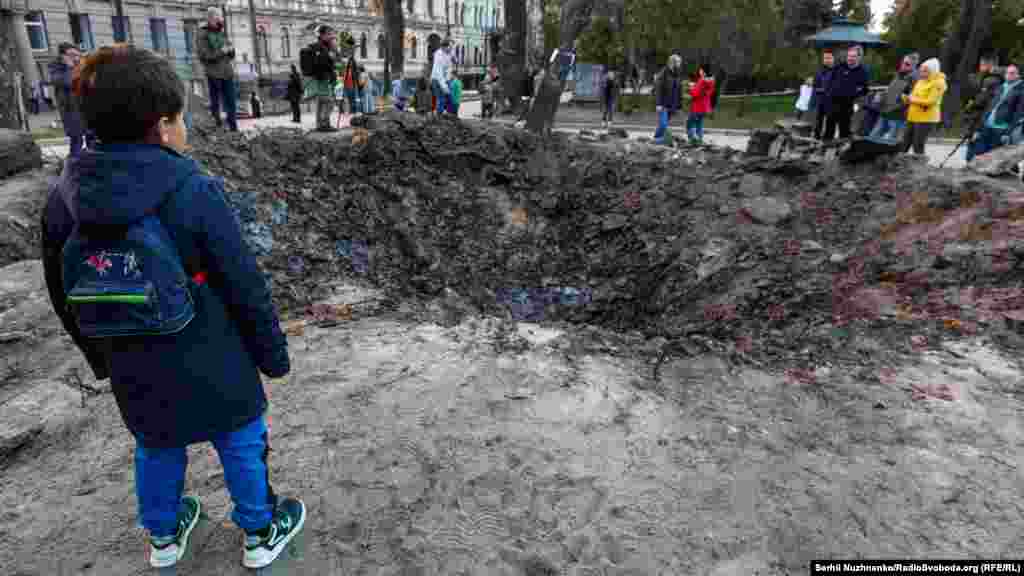 Egy kisfiú egy hatalmas krátert figyel a kijevi Tarasz Sevcsenko parkban lévő játszótér közelében. Az emberek később virágokat helyeztek el a mélyedésben a támadásban elhunytak emlékére