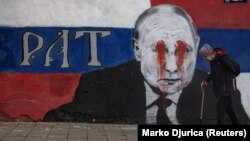 O femeie în vârstă merge pe lângă o pictură murală a președintelui rus Vladimir Putin, care a fost vandalizată cu vopsea roșie și cu cuvântul război scris în locul textului original „frate”, Belgrad, Serbia, 29 aprilie 2022.