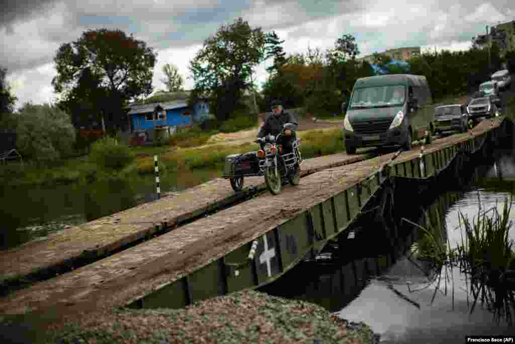 Locals and army vehicles cross a temporary bridge in Izyum that replaced one nearby which had been destroyed.&nbsp;