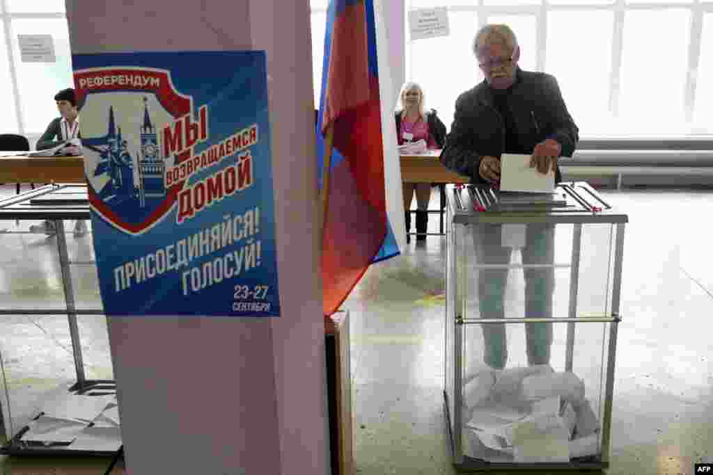 Egy férfi leadja szavazatát a referendumon egy mariupoli szavazóhelyiségben 2022. szeptember 27-én. &bdquo;Hazatérünk&rdquo; &ndash; hirdeti a plakát