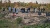 Polițiști și experți criminaliști examinează o groapă comună descoperită în regiunea Donețk din Ucraina în octombrie 2022.