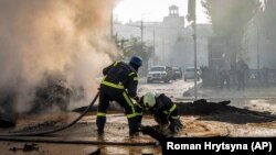 A firefighter helps his colleague to escape from a crater as they extinguish smoke from a burning car after a Russian attack in Kyiv on October 10.