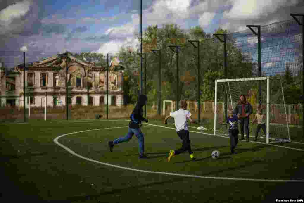 Boys play soccer next to a destroyed school in Izyum on October 3.&nbsp;After the city was recaptured from Russian forces in early September, a mass burial site with 440 graves was found and is being examined by experts.