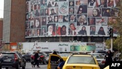 Iranianët kalojnë pranë një billbordi të madh që fotografi me fytyrat e grave të titulluar "Gratë e tokës sime". Aty shfaqen gra të cilat respektojnë hixhabin. Teheran, 13 tetor 2022. 