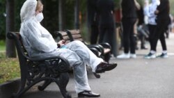 Девушка в защитном костюме сидит на скамейке на одной из улиц города.