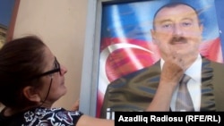 An Azerbaijani woman with an election poster for incumbent President Ilham Aliyev