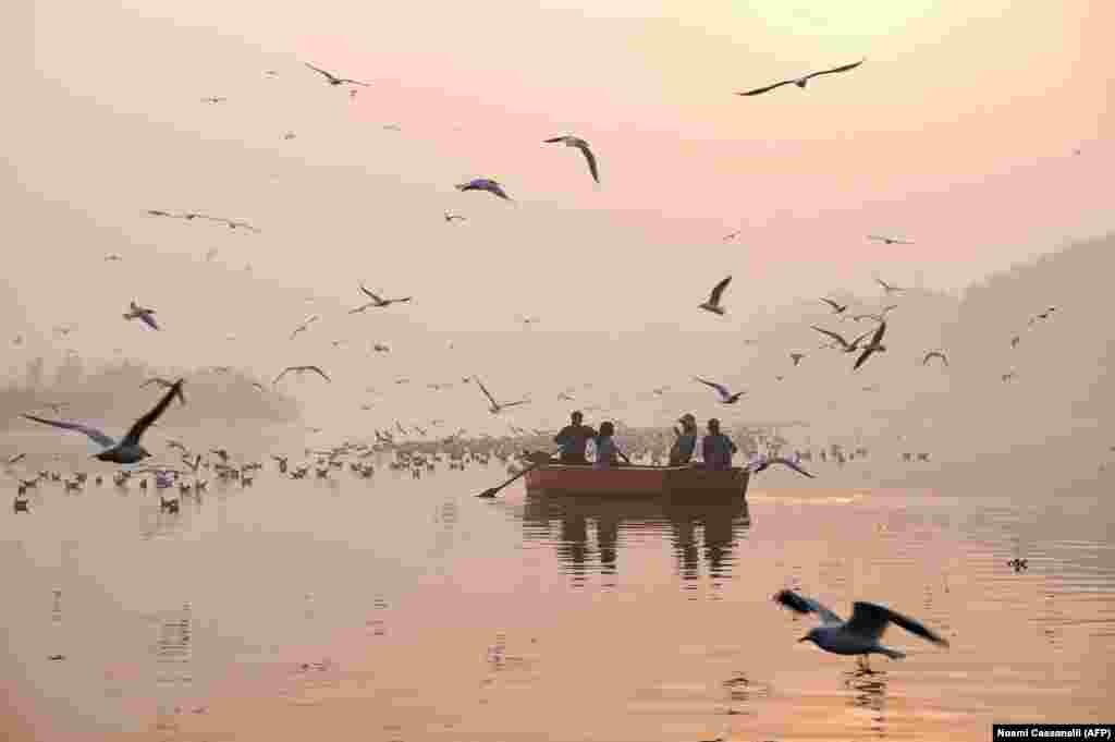 Indian women take pictures on a boat as migratory birds fly overhead on the Yamuna River on a morning of heavy air pollution in New Delhi. (AFP/Noemi Cassanelli)