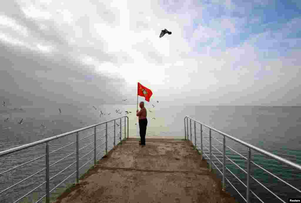 A man holds a Soviet flag as he stands on a pier during the opening of the cold-water swimming season in the Black Sea town of Saky, Crimea, on November 24. (Reuters/Pavel Rebrov)