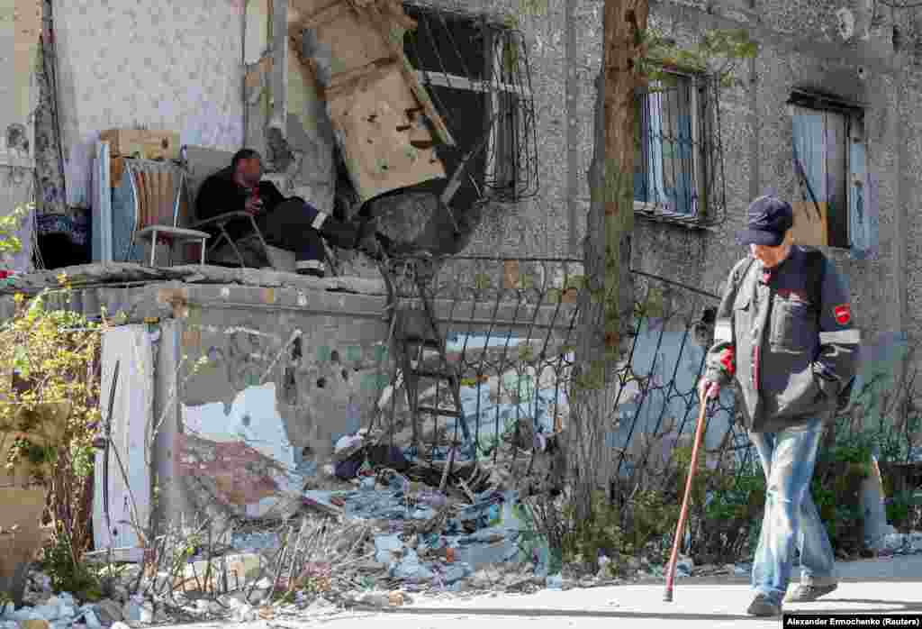 A man sits in an armchair outside a damaged residential building on May 12. After surviving months of shelling, residents must contend with queuing for limited water and food in the occupied city.