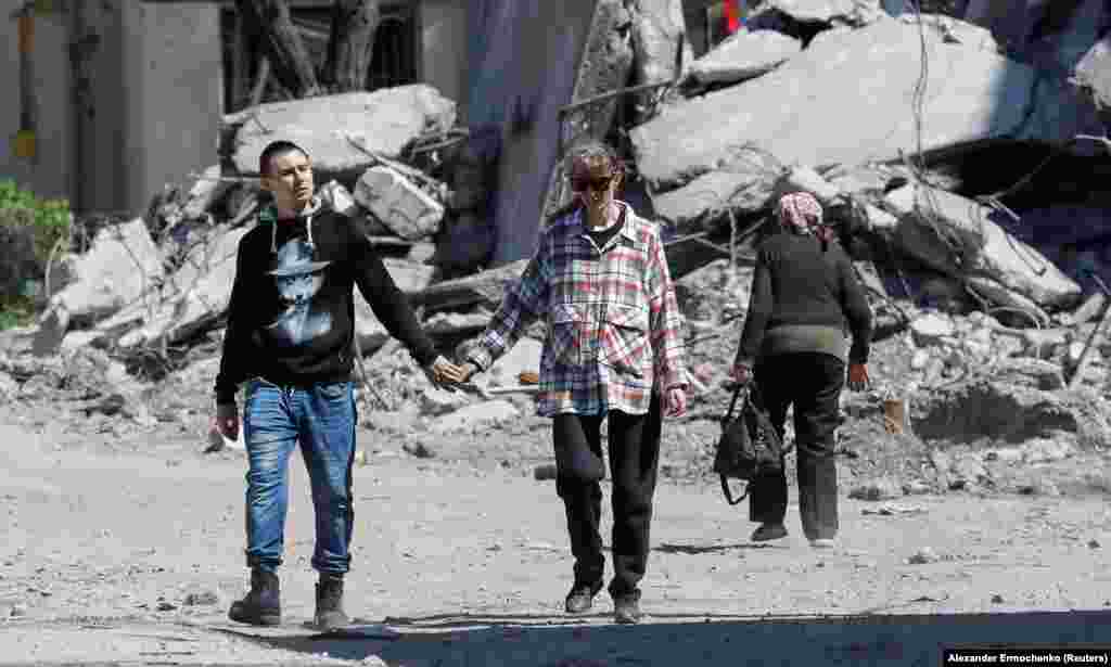 Брачен пар шета рака под рака низ уништена станбена зона на 12 мај.