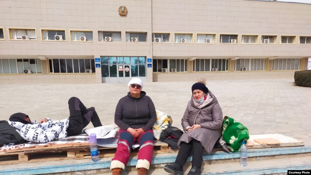 Жительницы Амангуль Жаппасова и Айболган Базарбаева (слева), объявившие голодовку, сидят на импровизированном лежаке перед зданием акимата Жанаозена. 31 марта 2022 года