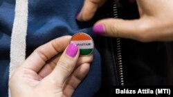 Az első választóknak járó nemzeti színű, „Szavaztam!” feliratú kitűzőt tűzik fel egy fiatal férfi pulóverére a nyíregyházi Vasvári Pál Gimnáziumban kialakított szavazókörben 2022. április 3-án. 