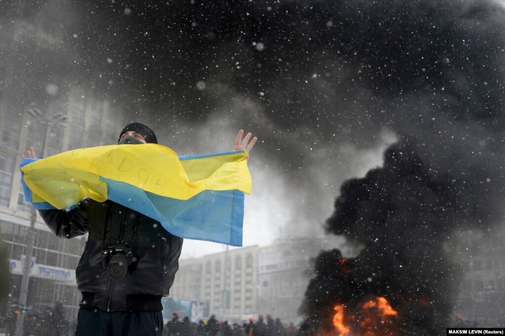 Një burrë duke mbajtur një flamur ukrainas, teksa tymi ngrihej në prapavijë, gjatë përleshjeve ndërmjet policisë dhe protestuesve proevropianë në Kiev, më 22 janar 2014.