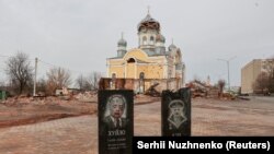 Pietre funerare cu portretele lui Vladimir Putin și Alexander Lukașenko în fața unei biserici avariate de bombardamente, în orașul Malin, regiunea Jitomir, 30 martie 2022.