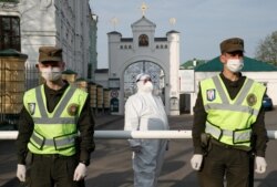 A Ukrainian health worker wearing protective gear stands next to members of the country's National Guard at the entrance to Kyiv's Pechersk Lavra monastery, where multiple cases of COVID-19 have been confirmed.