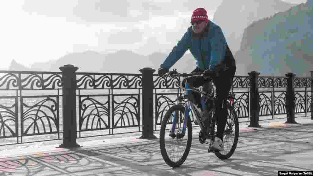Мужчина едет на велосипеде по набережной Судака