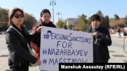 Пришедшие на площадь в Алматы в день анонсированного митинга держат плакат с требованием ввести санкции против экс-президента Назарбаева и главы КНБ Масимова, 23 октября 2021 года
