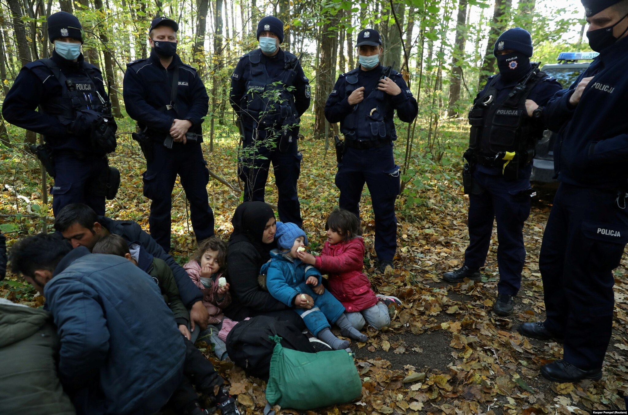 An Iraqi migrant woman and her children sit on the ground in Hajnowka, surrounded by Polish border guards and police officers on October 14.