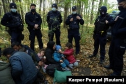 An Iraqi migrant woman and her children sit on the ground in Hajnowka, surrounded by Polish border guards and police officers on October 14.