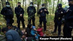 Rendőrök, illetve iraki bevándorlók gyerekeikkel a belarusz határ térségében lévő Hajnówka közelében 2021. október 14-én