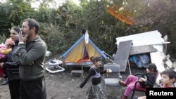 A Romany family from Romania stand near their tent shelter after police removed their caravan overnight in an illegal camp in Lesquin, near Lille. France insists it has acted legally.