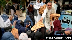 افراد بی بضاعت در مقابل یک خبازی تجمع کرده اند که مرد افغان به آنها نان خشک رایگان توزیع می کند. 