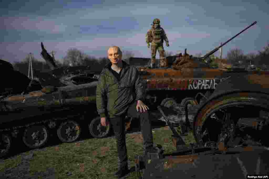 A man poses wearing a mask of Russian President Vladimir Putin while a Ukrainian soldier stands on top of a destroyed Russian tank in Bucha, on the outskirts of Kyiv, on April 7.