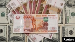 Пятитысячные рублевые банкноты на фоне стодолларовых банкнот