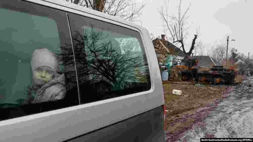 A child looks out the window of an evacuation vehicle near a destroyed Russian armored vehicle.
