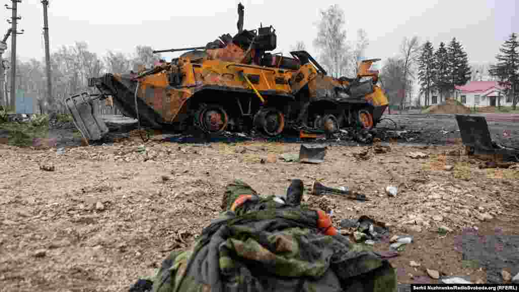 The body of a dead Russian soldier lies on the ground near the burned remains of an armored personnel carrier.