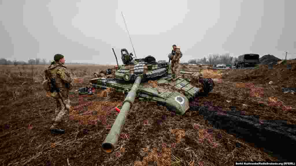 Украински войници инспектират руски танк, заседнал в калта.