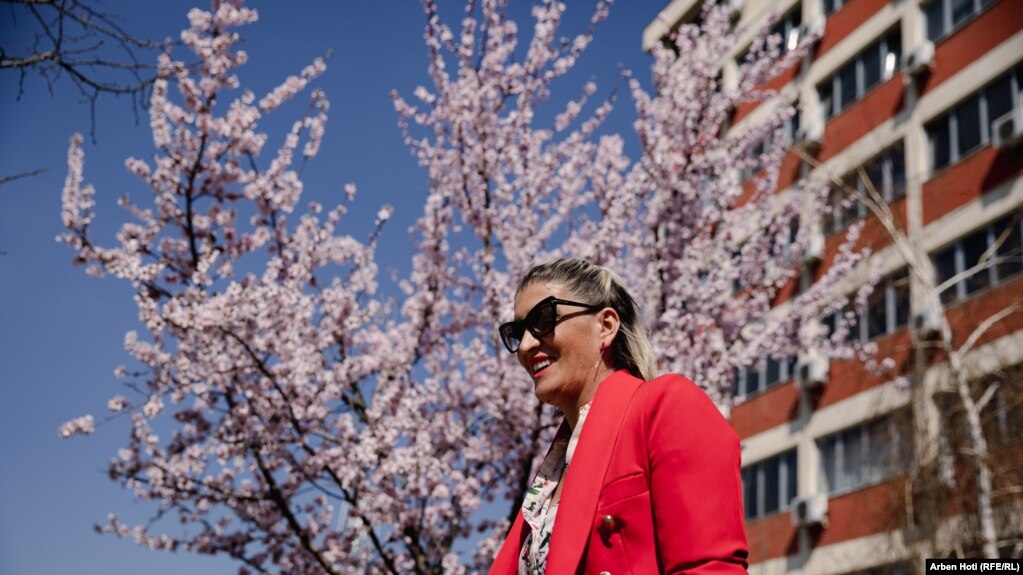 Një grua e buzëqeshur me një prapavijë peme të lulëzuar. 