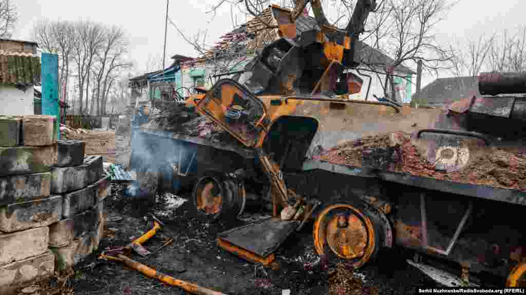 A smoldering Russian armored vehicle lies in ruins near a home.