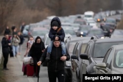 Refugiații ucraineni merg printre mașinile care stau la coadă pentru a trece granița din Ucraina în Moldova, la punctul de trecere a frontierei Mayaky-Udobne, pe 26 februarie 2022, la două zile după ce Rusia și-a lansat invazia.