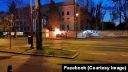 A car is seen on fire after crashing into the fence surrounding the Russian Embassy in Bucharest.