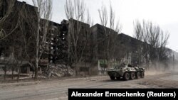 UKRAINE - An armoured vehicle of pro-Russian troops drives along a street past a residential building destroyed during Ukraine-Russia conflict in the besieged southern port city of Mariupol, Ukraine March 31, 2022.