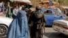 Taliban forces on patrol in Kabul with a woman in a burqa in the foreground.