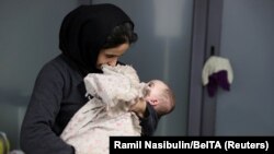 A woman holds a child as migrants gather for their departure to Iraq at the airport in Minsk on November 26.