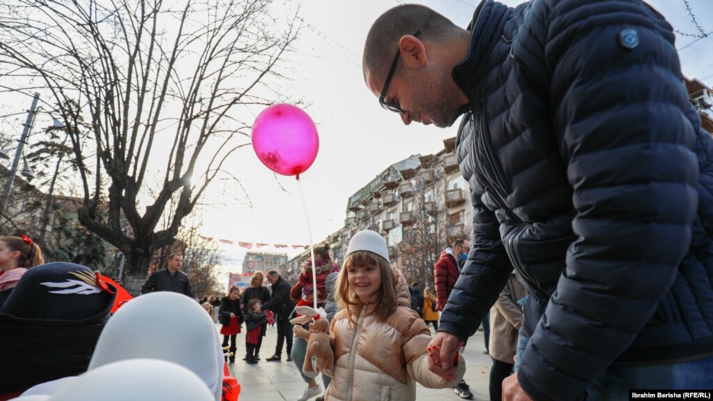 Një prind me vajzën e tij qëndrojnë pranë një tezge, ku janë vendosur disa plisa. Prishtinë, 28 nëntor 2021. 