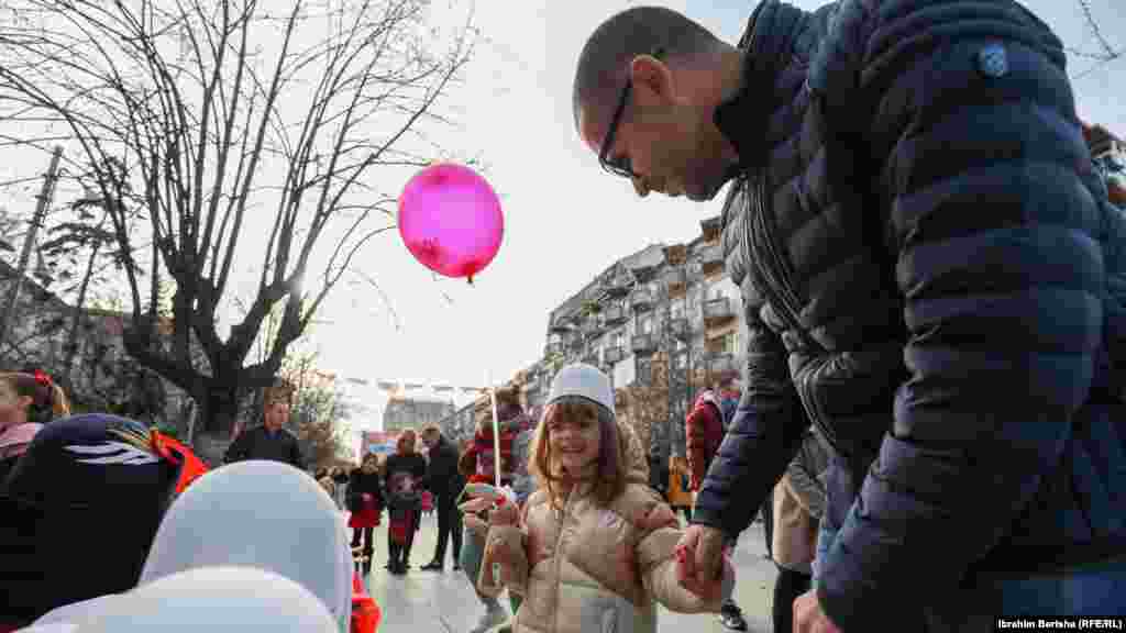 Një prind me vajzën e tij qëndrojnë pranë një tezge, ku janë vendosur disa plisa. Prishtinë, 28 nëntor 2021.&nbsp;