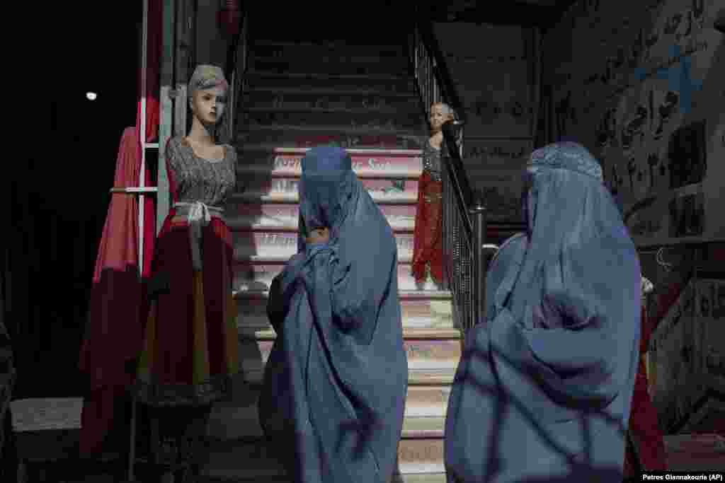 Burka-clad Afghan women walk past a clothing shop in Herat, Afghanistan.&nbsp;