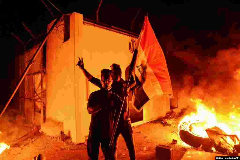 Iraqi demonstrators gesture as flames start consuming Iran's consulate in the southern Iraqi Shi'ite holy city of Najaf on November 27. (AFP/Haidar Hamdani)