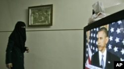 A veiled woman walks near a television in the West Bank city of Nablus during the May 19 speech by U.S. President Barack Obama.