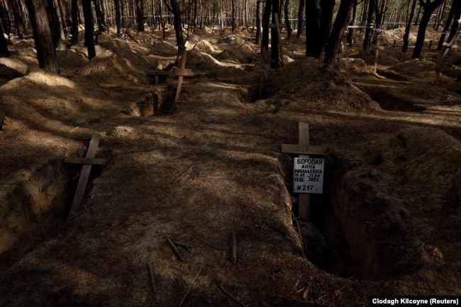 A cross lies in the empty grave of a person exhumed from an improvised cemetery in Izyum, Kharkiv region, on October 19.