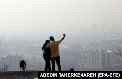 Iranski par snima selfi dok smog zaklanja horizont u Teheranu.