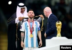 Lionel Messi este îmbrăcat cu mantia neagră, înainte să primească trofeul Cupei Mondiale din partea emirului Qatarului, șeicul Tamim bin Hamad Al Thani, și a președintelui FIFA, Gianni Infantino, 18 decembrie 2022.