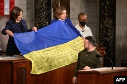 Volodimir Zelenski oferă un drapel național ucrainean președintei Camerei Reprezentanților, Nancy Pelosi, și vicepreședintei Kamala Harris, în timpul discursului său în Congresul SUA, 21 decembrie 2022.