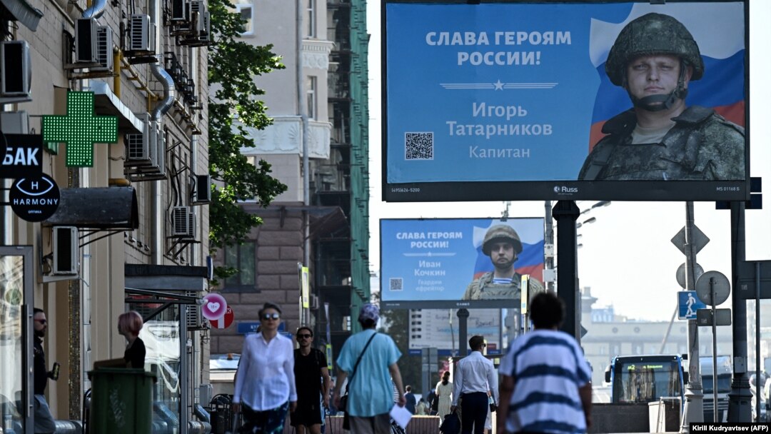 Oamenii trec pe lângă panouri publicitare care prezintă soldați ruși, cu sloganul „Glorie eroilor Rusiei”, pe o stradă din Moscova, august 2022.
